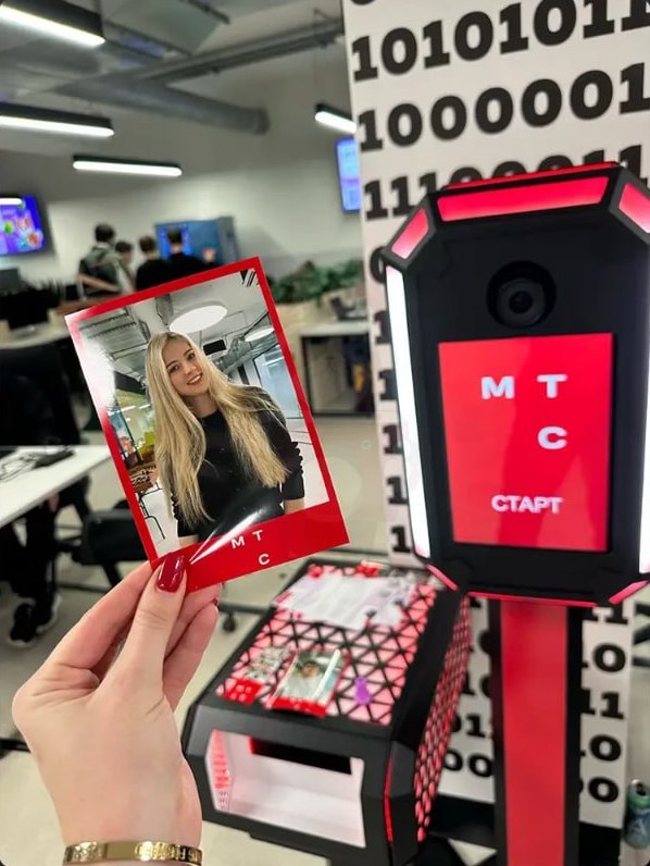 Гостья держит карточку с готовым портретом рядом со стойкой